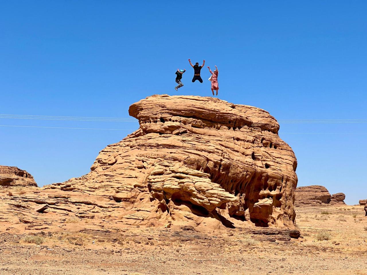Travellers jumping on a sandstone formation in Saudi Arabia